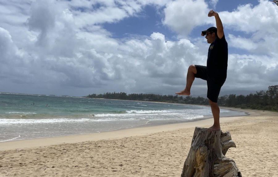 Anthony balancing on a driftwood stump on an empty beach