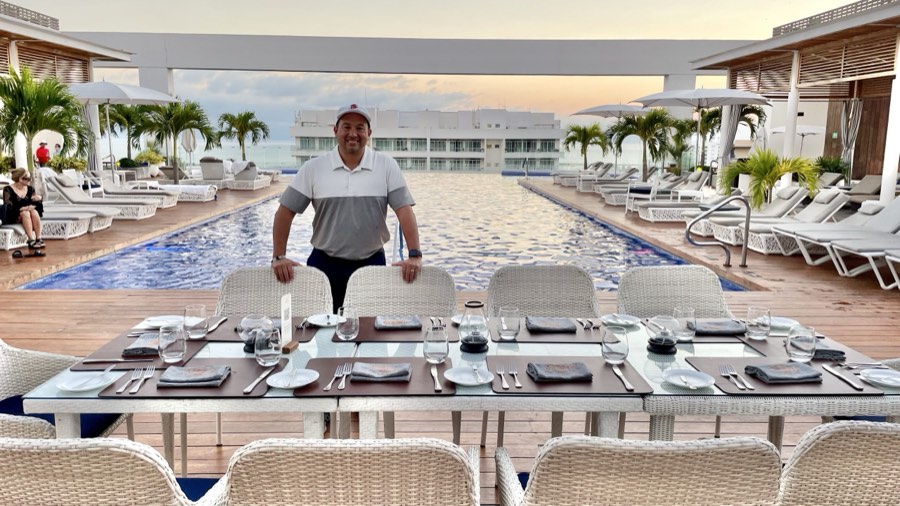 Long dinner table set beside a resort pool at sunset